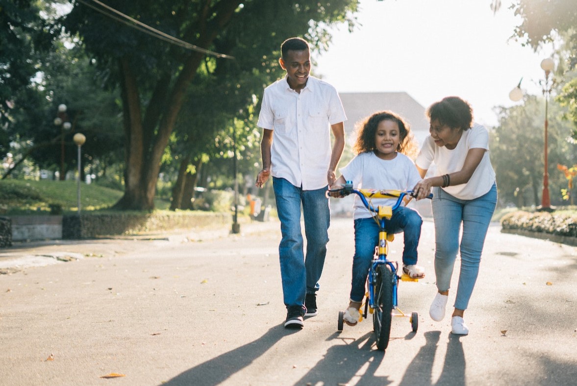parents teaching girl to ride a bike